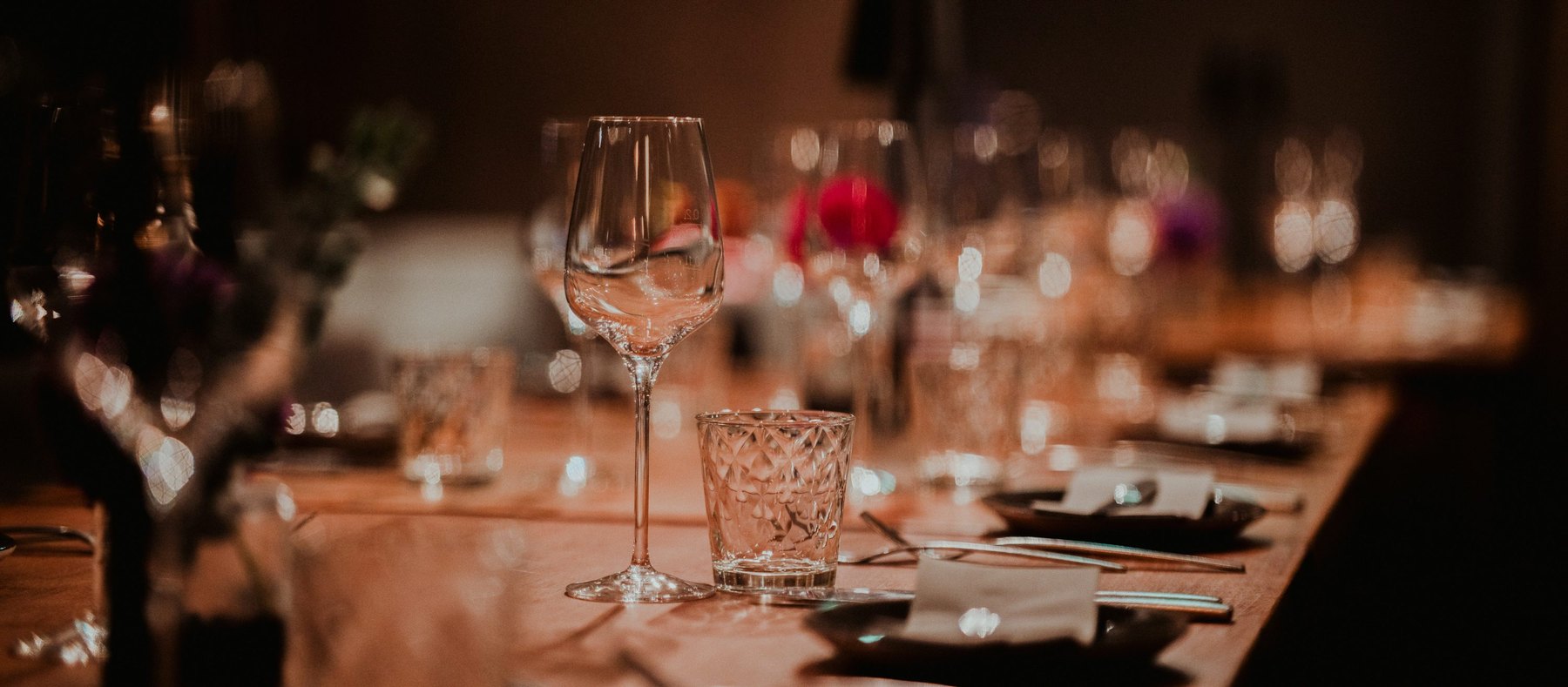Warm-lit wine glasses and place settings at a dinner table